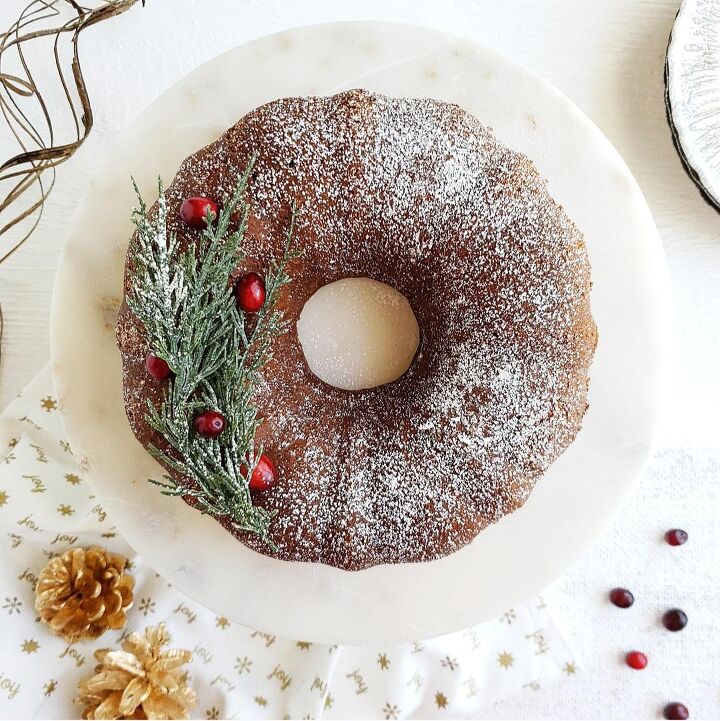 chocolate molasses crinkle cookies, functional image gingerbread bundt cake top down photo cake is garnished with snowy white powdered sugar evergreen twigs from a christmas tree and red cranberries background is styled with gold pinecones and a white marble cake plate