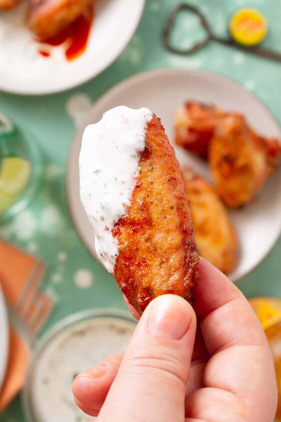 dry rub ranch chicken wings baked, womans hand holding a baked chicken wing that s been dipped in a white sauce