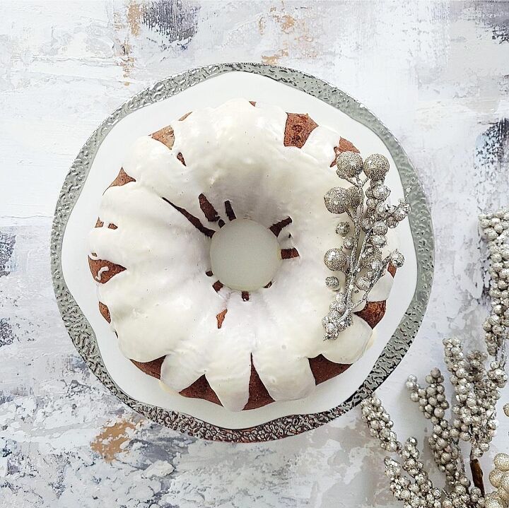 eggnog bundt cake, functional image eggnog cake top down on a silver rimmed cake stand cake is topped with a white eggnog drip glaze and decorated with silver baubles for christmas