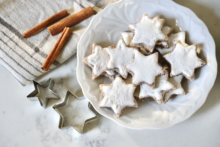 authentic german cinnamon star cookies zimtsterne, cinnamon star cookies on plate with star shaped cookie cutters and cinnamon sticks