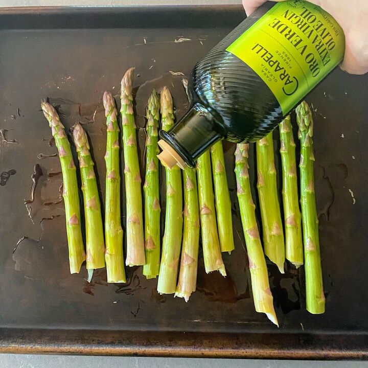 roasted asparagus with parmesan lemon, hand pouring olive oil onto baking sheet asparagus