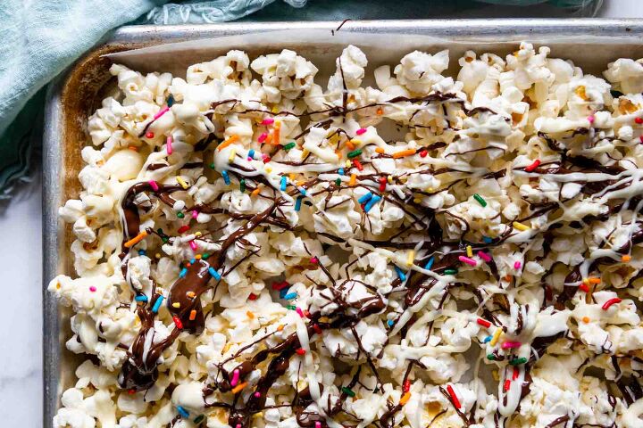 chocolate drizzled popcorn expert tips ideas, overhead shot of popcorn on baking sheet with chocolate and sprinkles