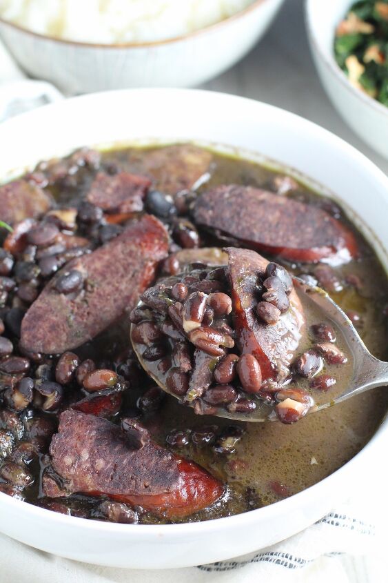 feijoada rice and beans brazilian style with meat, Serving spoon scooping up cooked black beans with pork sausage and beef in a white bowl Feijoada is rice and beans Brazilian style with pork sausages beef and more