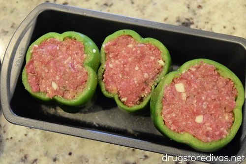 Three green peppers stuffed with a meatball mixture in a bread pan
