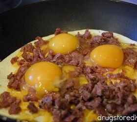 Three eggs on top of sausage on top of cheese on top of a tortilla in a pan