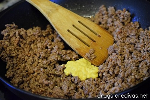 Ground beef and mustard in a pan with a bamboo spoon