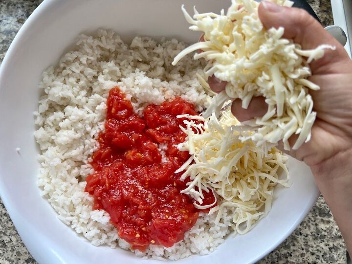 brazilian baked rice with cheese and tomatoes, Hand adding shredded mozzarella to crushed tomatoes and cooked rice in a bowl for Baked Rice with Cheese and Tomatoes