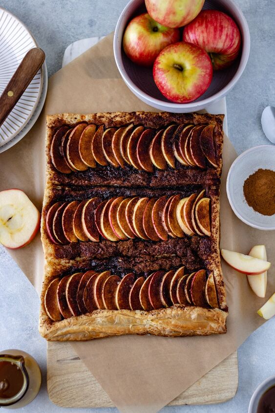honeycrisp apple tart with caramel sauce, A baked sheet of puff pastry topped with apple slices coconut sugar and cinnamon laying on a piece of parchment paper and a marble board