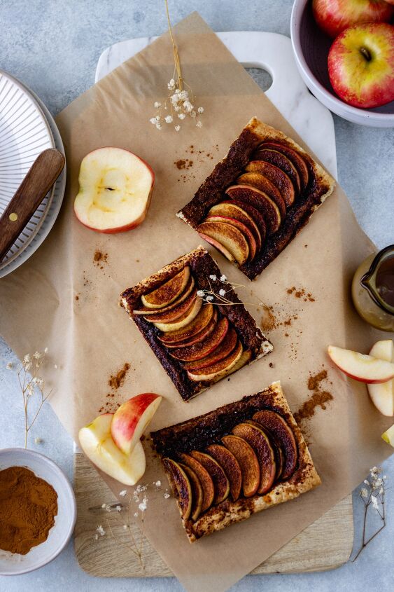honeycrisp apple tart with caramel sauce, Three mini apple tarts laying on a marble board surrounded by fresh apple slices and ground cinnamon