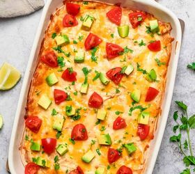 creamy chicken enchilada casserole, side angle shot of a taking a piece out of chicken enchilada casserole in a white baking dish with avocado and tomatoes