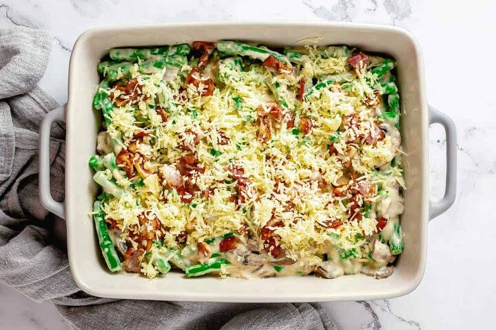 cheesy green bean casserole with bacon, Creamy mushroom sauce with green beans in a baking dish topped with crumbled bacon and grated cheddar cheese