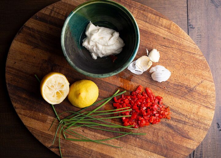 Bowl with mayonnaise on a cutting board with lemon halves chives roasted red peppers and garlic cloves
