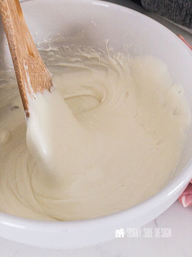 Wooden spoon stirring melted white baking chips in a white bowl