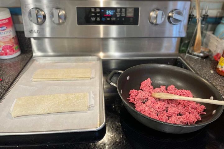 simple ground beef puff pastry recipe, Puff pastry on a baking sheet with parchment paper on the left and a skillet with raw ground beef beginning to cook with a wooden spoon on the right