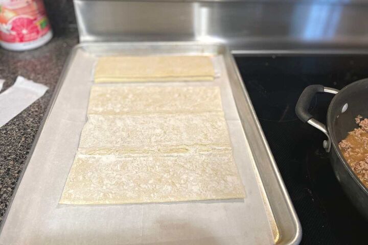 simple ground beef puff pastry recipe, Sheet of frozen puff pastry laid out on a baking sheet on top of parchment paper