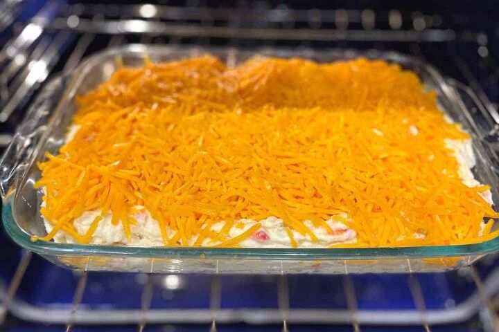 easy twice baked mashed potato casserole recipe, Easy Twice Baked Mashed Potato Casserole process photo showing the mashed potato casserole in a glass 9x13 baking dish covered in shredded cheese and ready to go in the oven