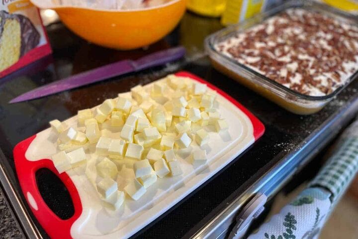 pumpkin crunch cake with yellow cake mix, cutting board with cubed butter on it next to the pumpkin crunch dish waiting for the butter to be put on top