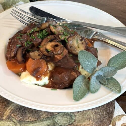 how to make delicious creamy tuscan sausage and bean soup, white bowl with raised dot edge fresh sage beef potatoes mushrooms silver fork silver knife