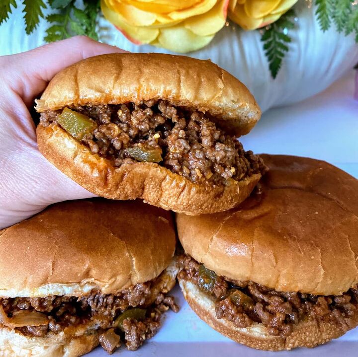 old fashioned sloppy joes recipe, hand holding sloppy joes and two sandwiches resting on a plate