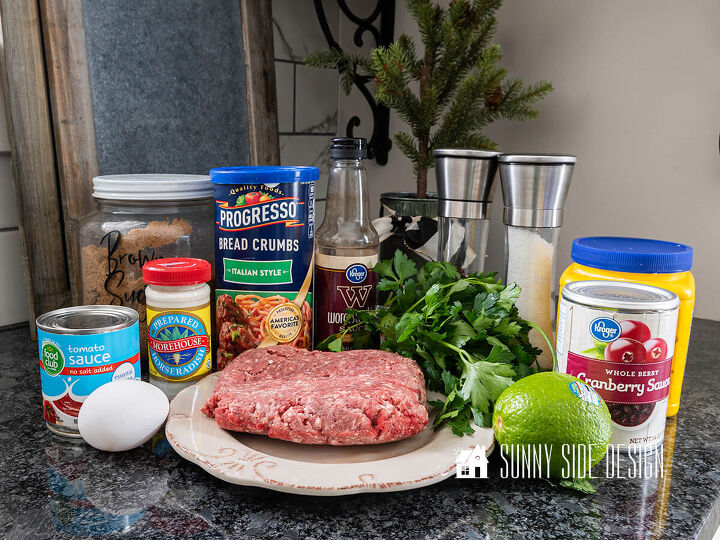 Ingredients for homemade meatball appetizer in a cranberry sauce Raw ground beef on a plate with parsley lime egg tomato sauce prepared horseradish brown sugar Italian bread crumbs Worcestershire sauce salt pepper whole berry cranberry sauce and cornstarch