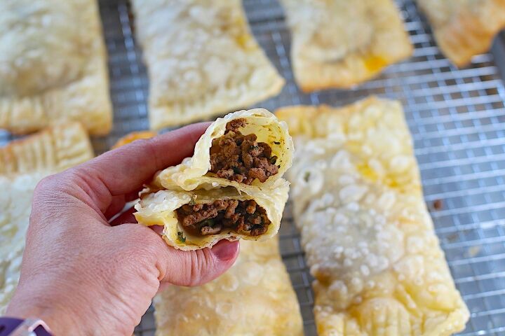 brazilian pastel recipe with beef filling, Hand holding two halves stacked of golden brown fried Pastel over sheet pan of more pasteis for traditional Brazilian Pastel Recipe with ground beef filling