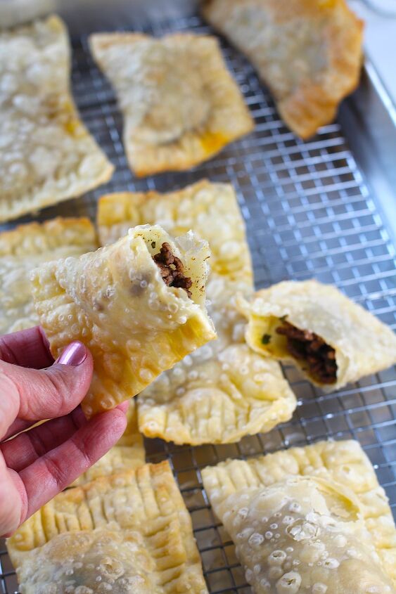brazilian pastel recipe with beef filling, Hand holding half of golden brown fried Pastel over sheet pan of more pasteis for traditional Brazilian Pastel Recipe with ground beef filling