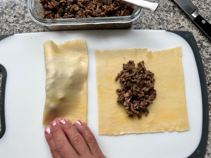 brazilian pastel recipe with beef filling, Fingers pressing the edges of the folded pastel dough with a second pastel laying open next to it with filling on top for Brazilian Pastel recipe