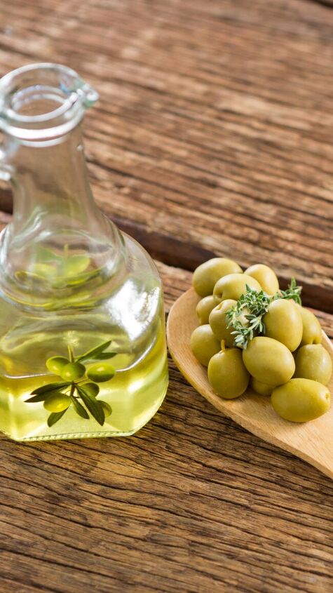 cruet of olive oil next to a wooden spoon filled with green olives