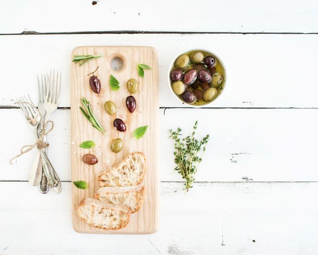 wooden serving bowl with green and greek olives and herbs