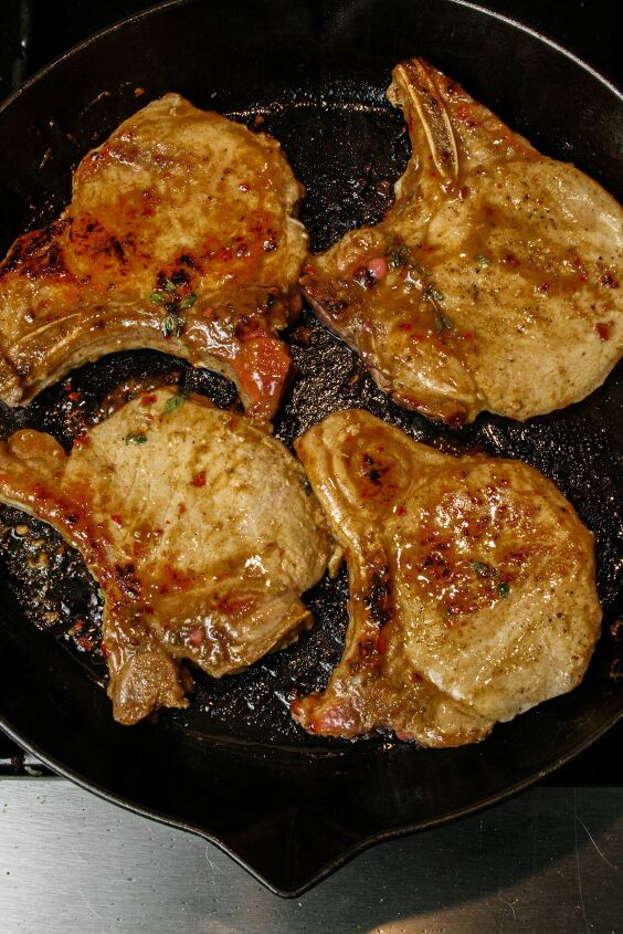 pan seared maple pork chops, Pan Seared Maple Pork Chop photographed cooking in a cast iron Staub skillet the skillet is black there is a maple sauce on the pork chops