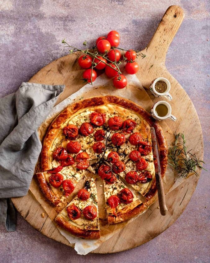 roasted cherry tomatoes tart with cheese, Cherry Toamoes Tart on parchment paper and wooden board with a knife resting on top and tomatoes off to side