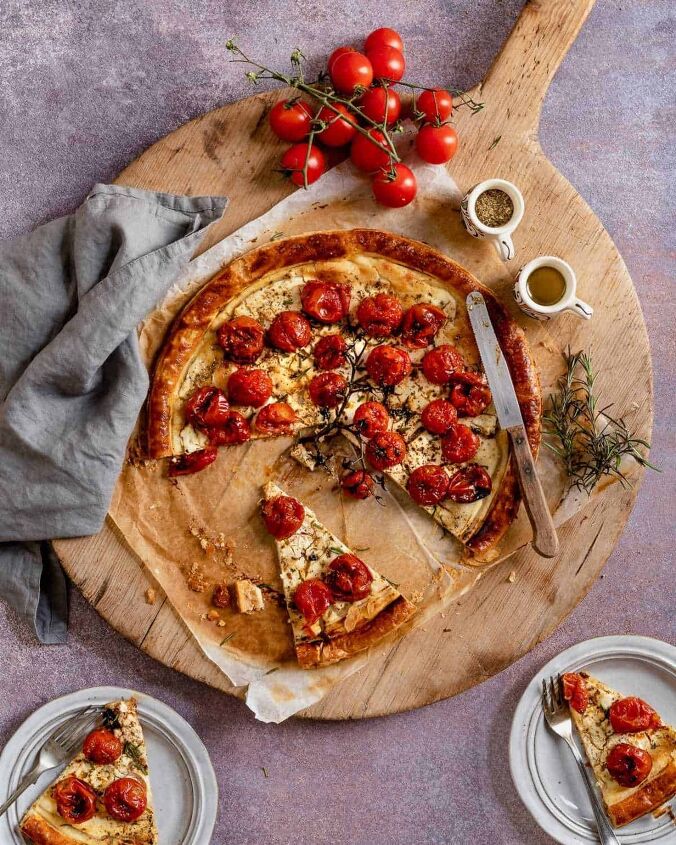roasted cherry tomatoes tart with cheese, Cherry Tomatoes Tart on parchment paper and a wooden board with a knife resting on top and tomatoes off to the side and two slices on the plates