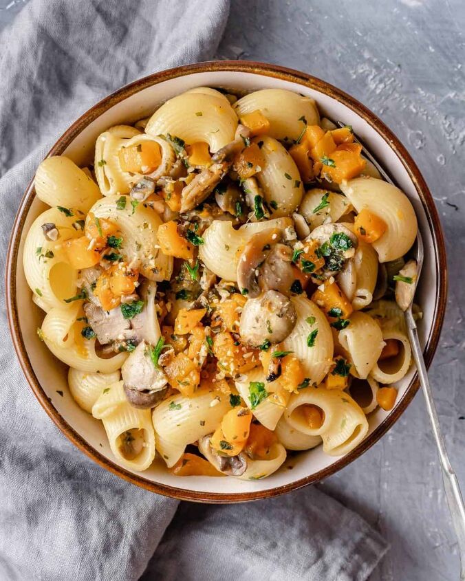 pumpkin and mushrooms pasta, A close up of a pasta bowl with a fork showing pasta with pumpkin cubes mushrooms seeds and fresh herbs