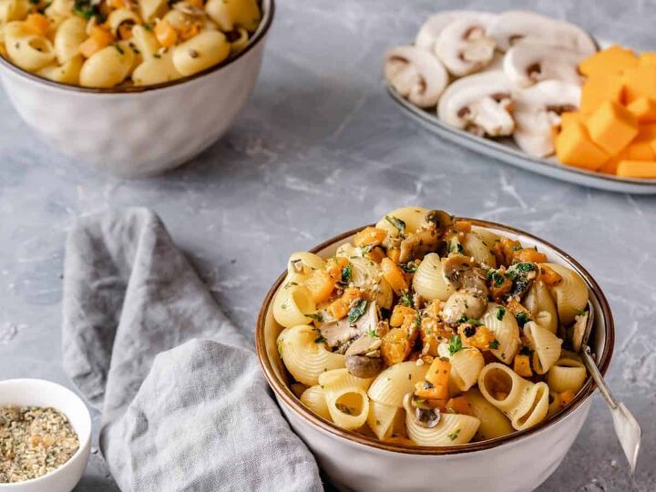 pumpkin and mushrooms pasta, Two bowls of Pasta on a grey table The bowls show pasta with pumpkin cubes mushrooms seeds and fresh herbs In the background some ingredients