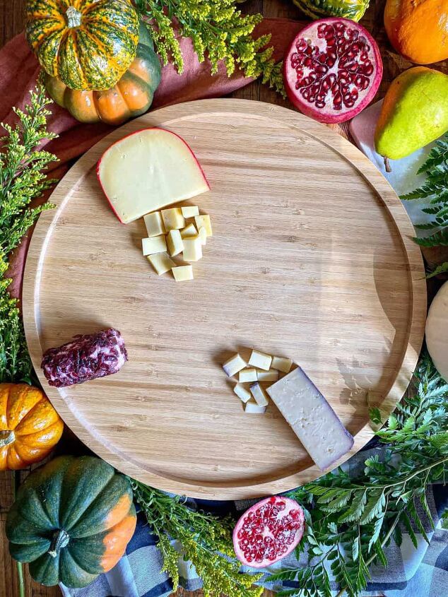 fall charcuterie board happy honey kitchen, Three different types of cheese are on a round wooden board Greenery and fresh pumpkins surround the board
