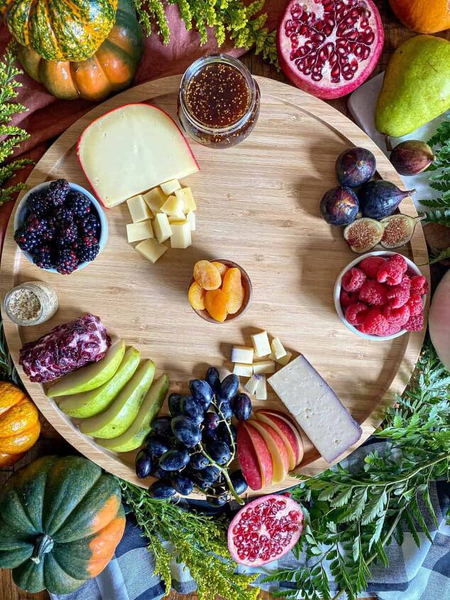 fall charcuterie board happy honey kitchen, Three different types of cheese and variety of fruit are on a round wooden board Greenery and fresh pumpkins surround the board