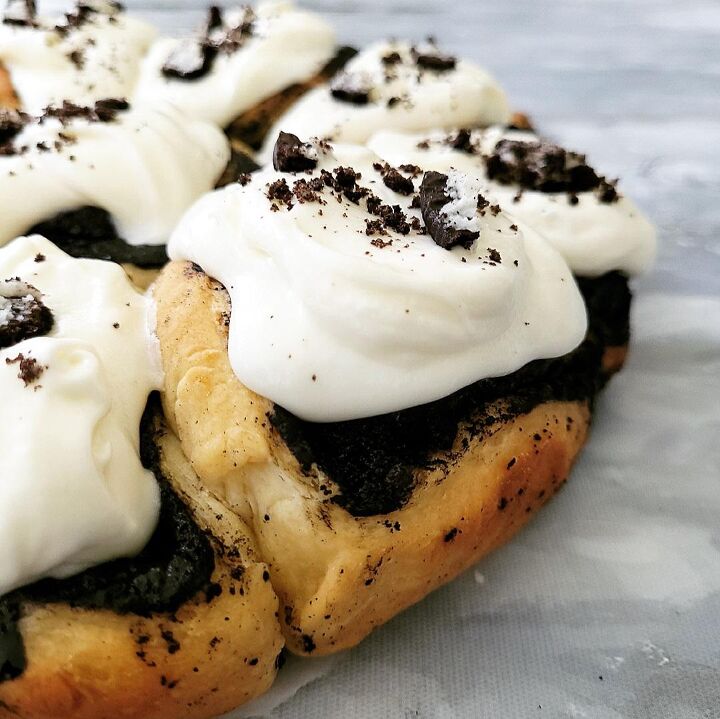 oreo cinnamon rolls, oreo cinnamon rolls close of of rolls with cream cheese icing and oreo cookie crumbs on top rolls are in the circular pattern of their baking pan and are uncut background is gray