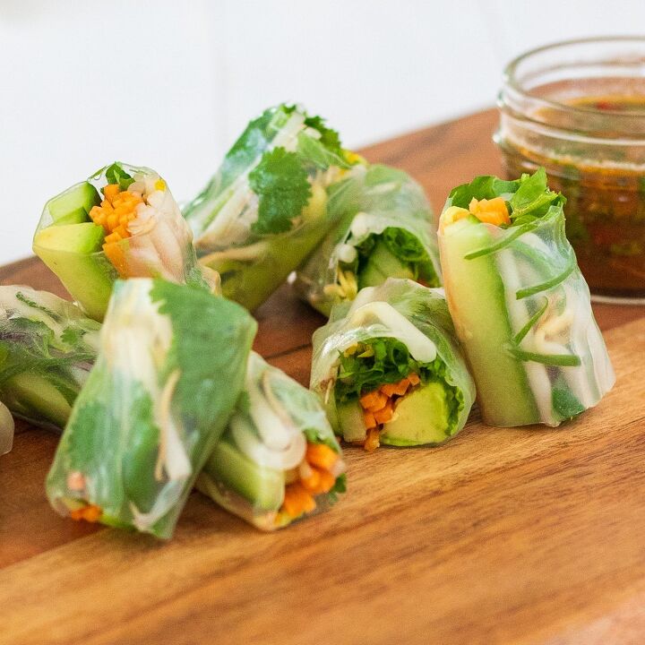 Rice paper rolls cut in half served on wooden board with dressing