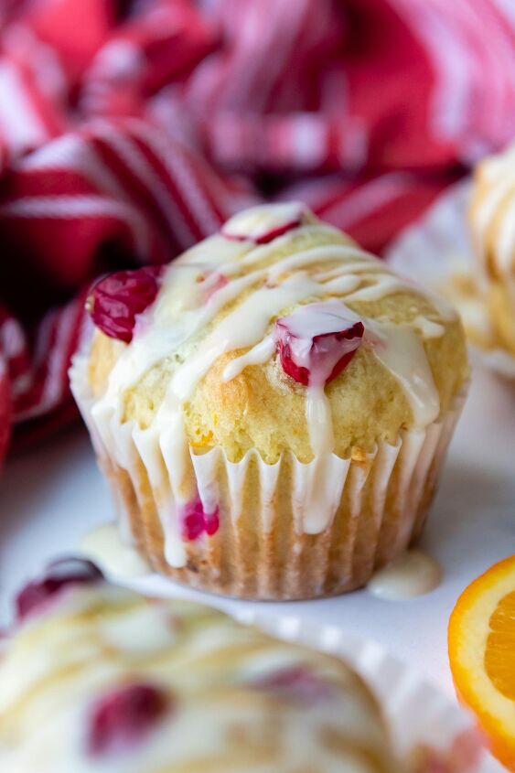 extra fluffy gluten free cranberry orange muffins, a whole cranberry muffin with glaze on top resting on a white marble surface