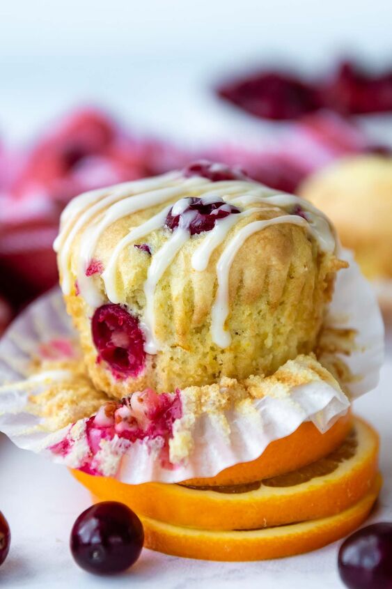 extra fluffy gluten free cranberry orange muffins, a cranberry muffin resting on sliced oranges with glaze on top