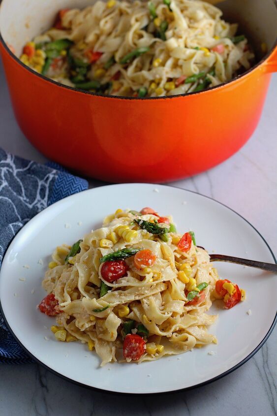 roasted vegetable pasta primavera recipe, Fresh Creamy Pasta Primavera Recipe on a plate with fork and pot in background on counter It has fettuccine parmesan cheese roasted asparagus carrots tomatoes and fresh corn kernels