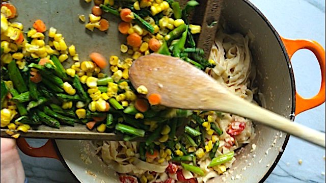 roasted vegetable pasta primavera recipe, Wood spoon scraping asparagus corn and carrots from a sheet pan into the pot of Creamy Pasta Primavera It has fettuccine parmesan cheese roasted asparagus carrots tomatoes and fresh corn kernels