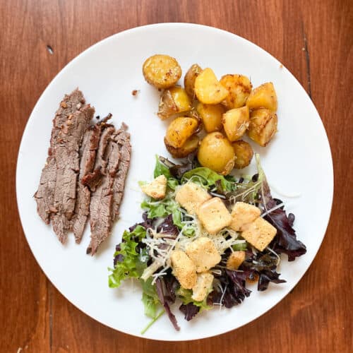 filet mignon with southwestern sauce, white plate on the table with marinated flank steak broasted potatoes and a salad