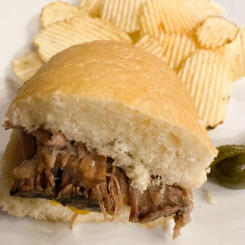 filet mignon with southwestern sauce, a 1 2 of a beef sandwich with potato chips on a white plate with pickles on the side This is such an easy slow cooker beef sandwich recipe