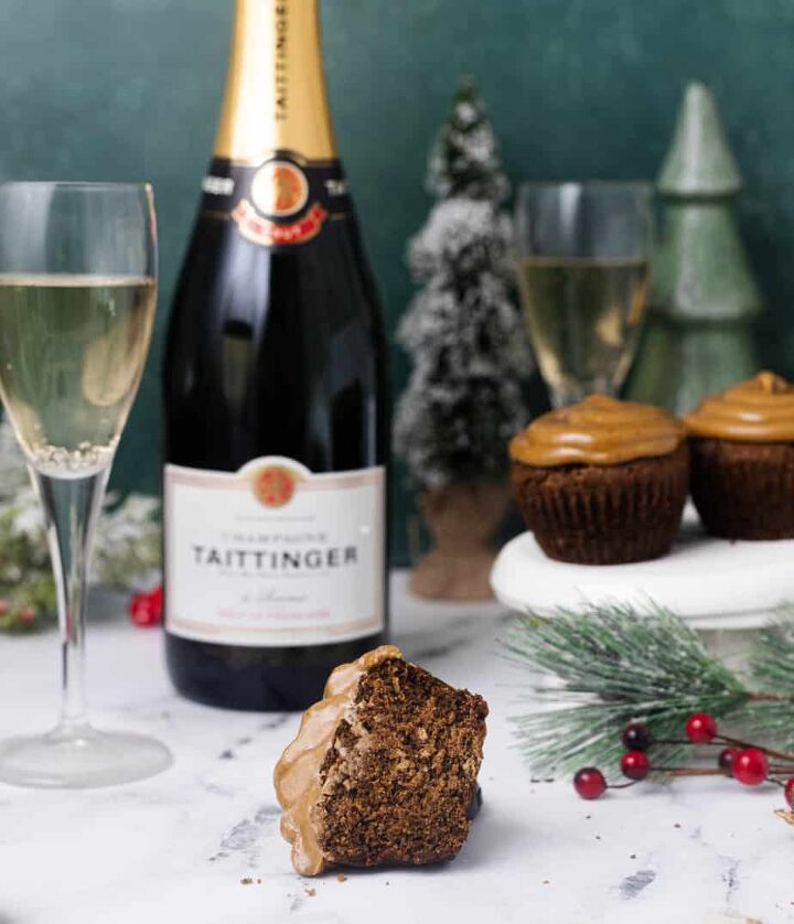 easy small batch gingerbread cupcakes, Gingerbread cupcake cut in half to show the inside and the frosting with greenery for christmas in the background as well as more cupcakes and a glass of brut with the bottle