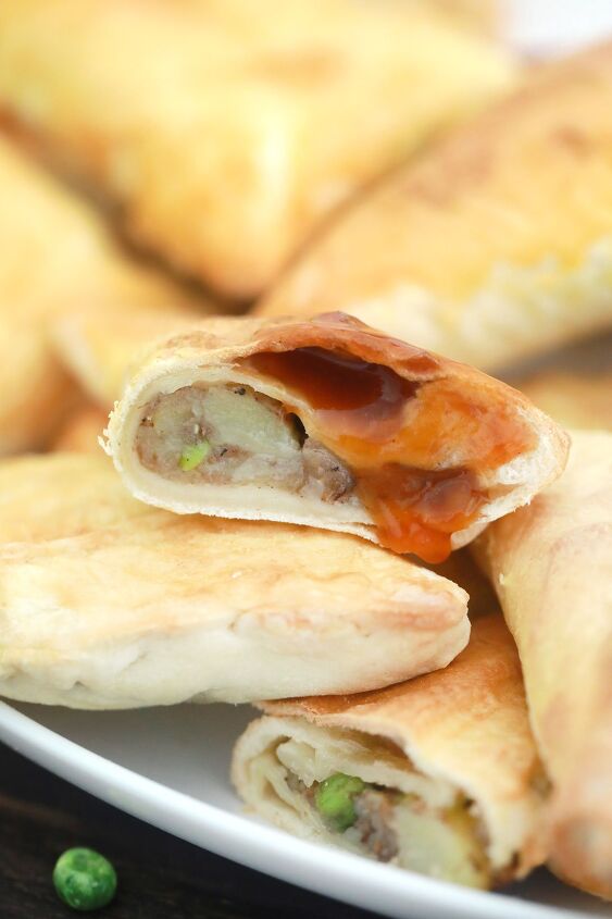 easy air fryer vegan samosas using spring roll wrappers, close up of a halved air fryer vegan smosa with tamarind chutney dripping off it