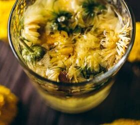 how to make calendula tea, bright yellow calendula flowers resting in a glass of water on a wooden table