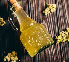 how to make elderflower cordial, fresh elderflower heads surround a glass sun bottle filled with golden syrup elder flower cordial recipe