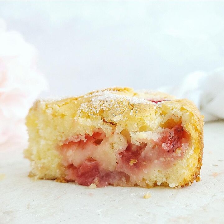 french strawberry cake, french strawberry cake side view of a single slice close up view to see the delicate crumb strawberries baked in and white sugar sprinkled on top background is pale blue and white