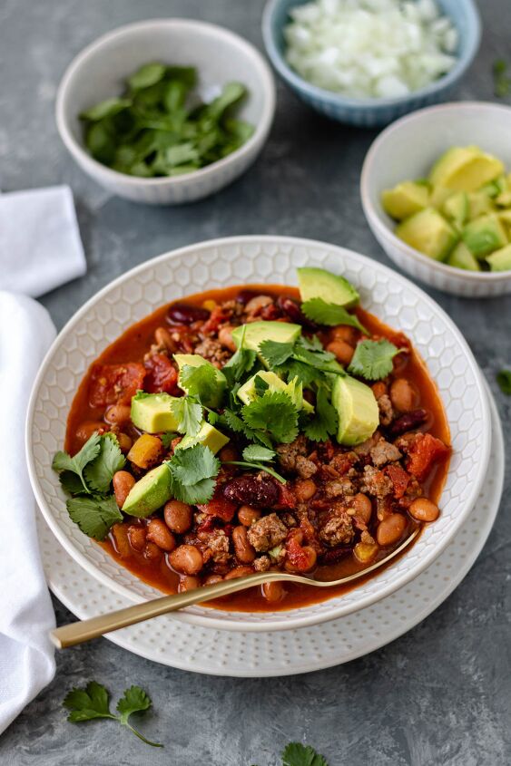30 minute chicken chipotle chili, A glass ceramic bowl filled with Chicken Chipotle Chili sitting on a plate and topped with avocado chunks and fresh cilantro